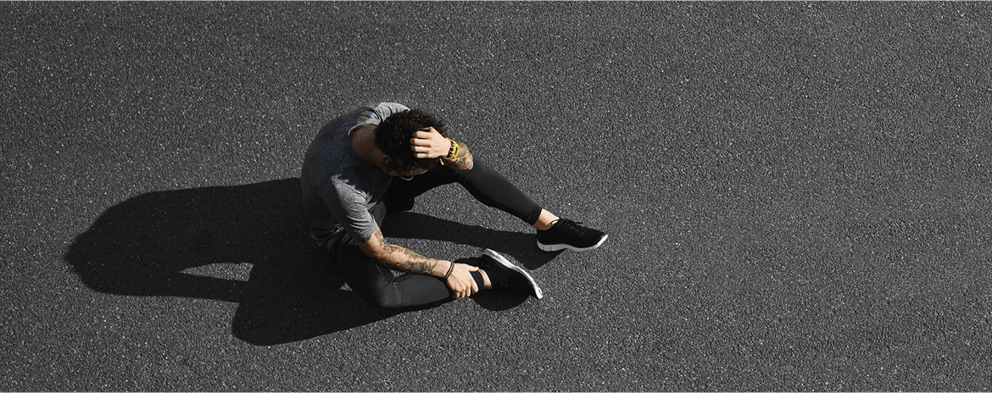 A male sitting on the ground holding his head.