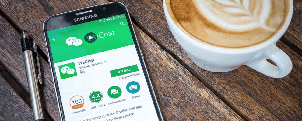 A phone with WeChat displayed on the screen next to a cup of coffee.